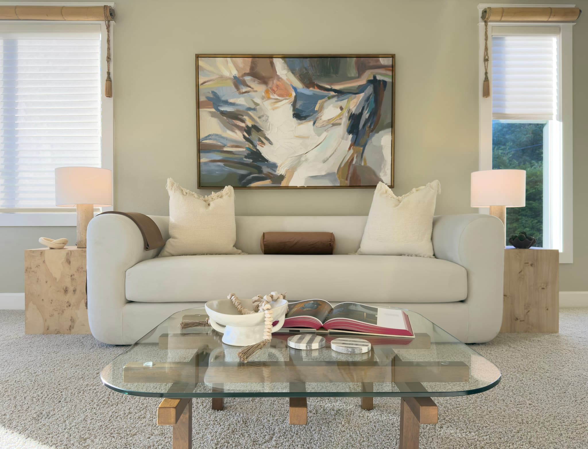 Staged living room in soft neutrals: a cream sofa beneath a large abstract painting, flanked by burl-wood side tables and lamps
