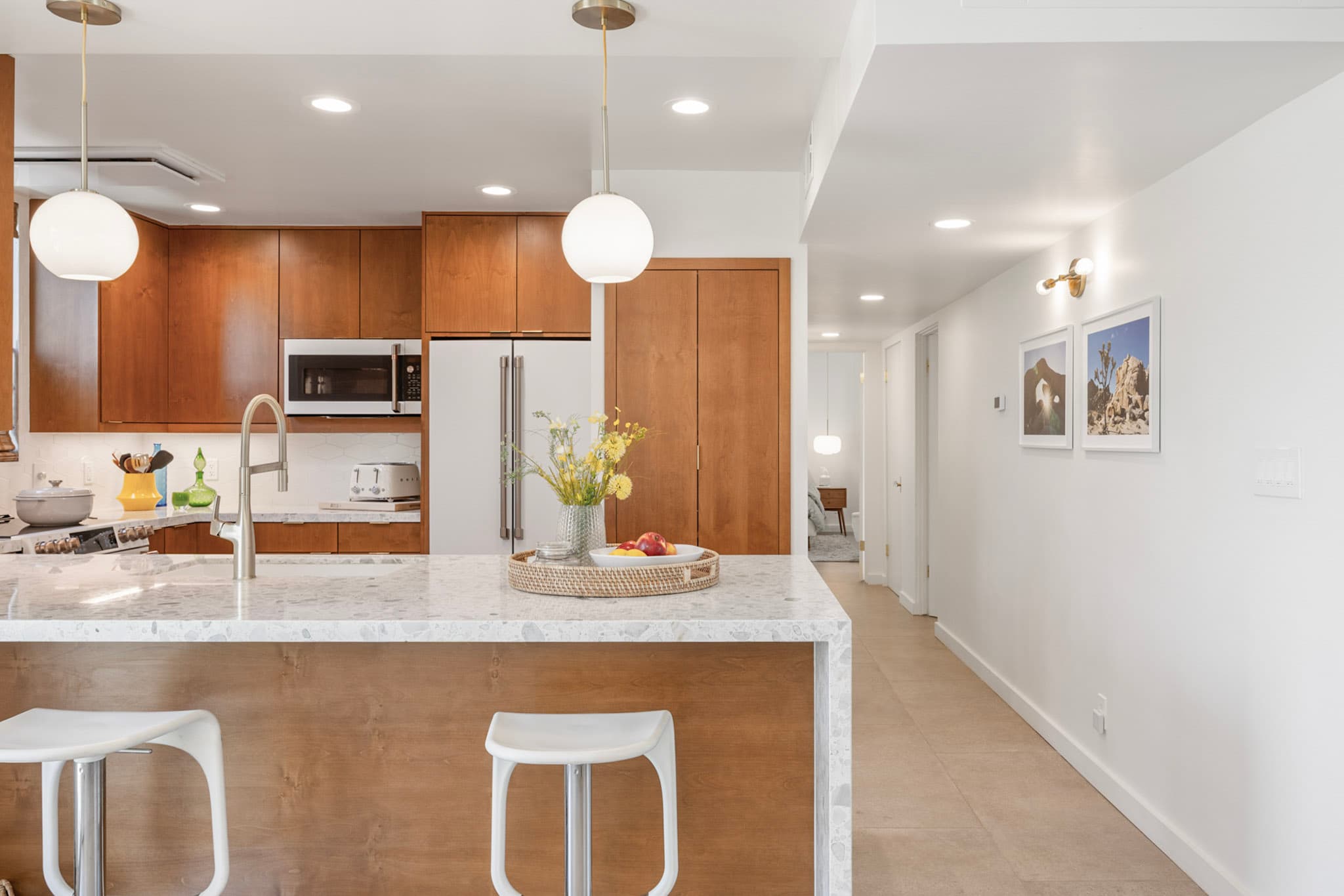 Remodeled Palm Springs kitchen with warm walnut cabinetry, a terrazzo waterfall peninsula and white globe pendants