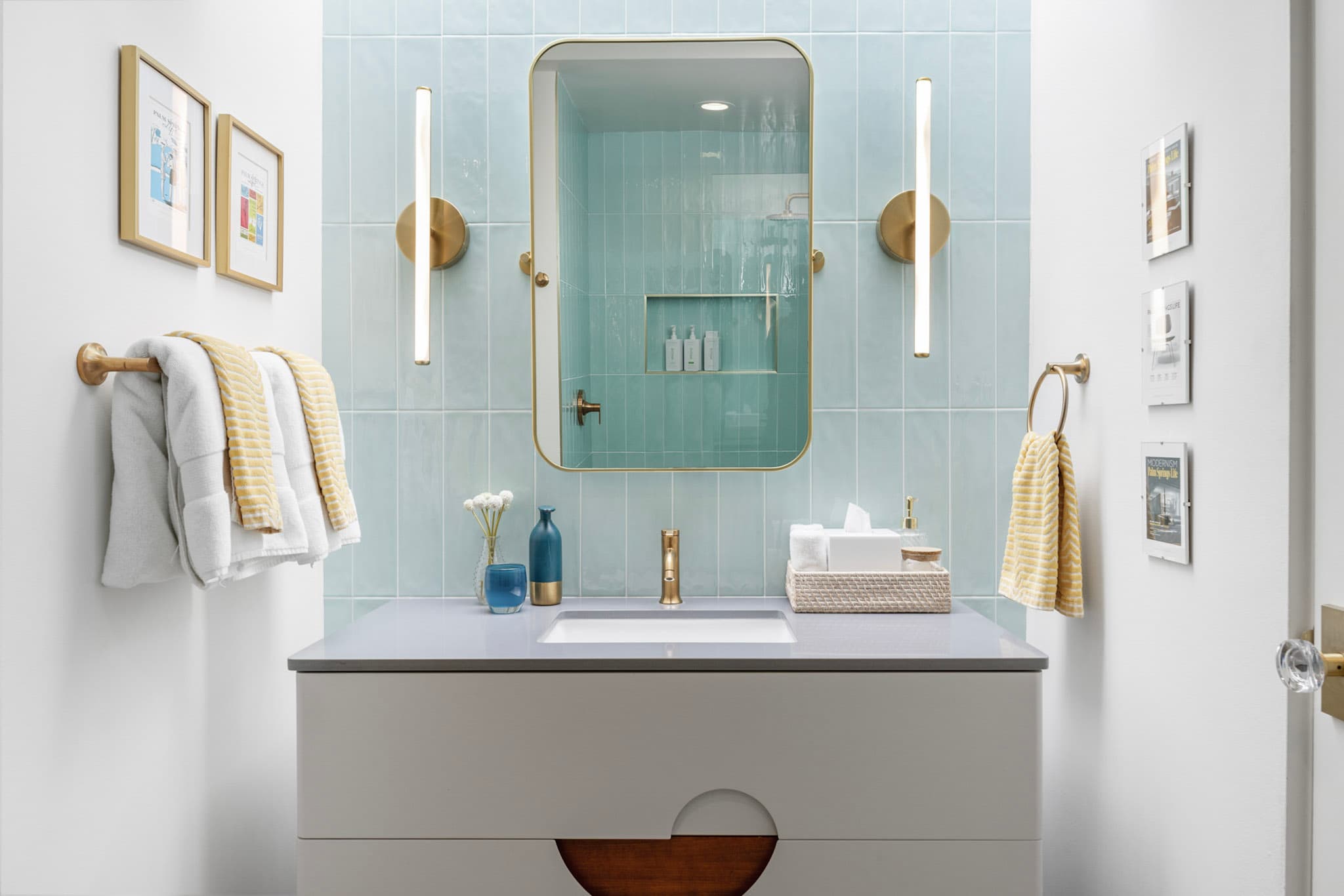 Remodeled Palm Springs bathroom with pale blue vertical tile, a brass-framed mirror and slim brass sconces above a floating vanity